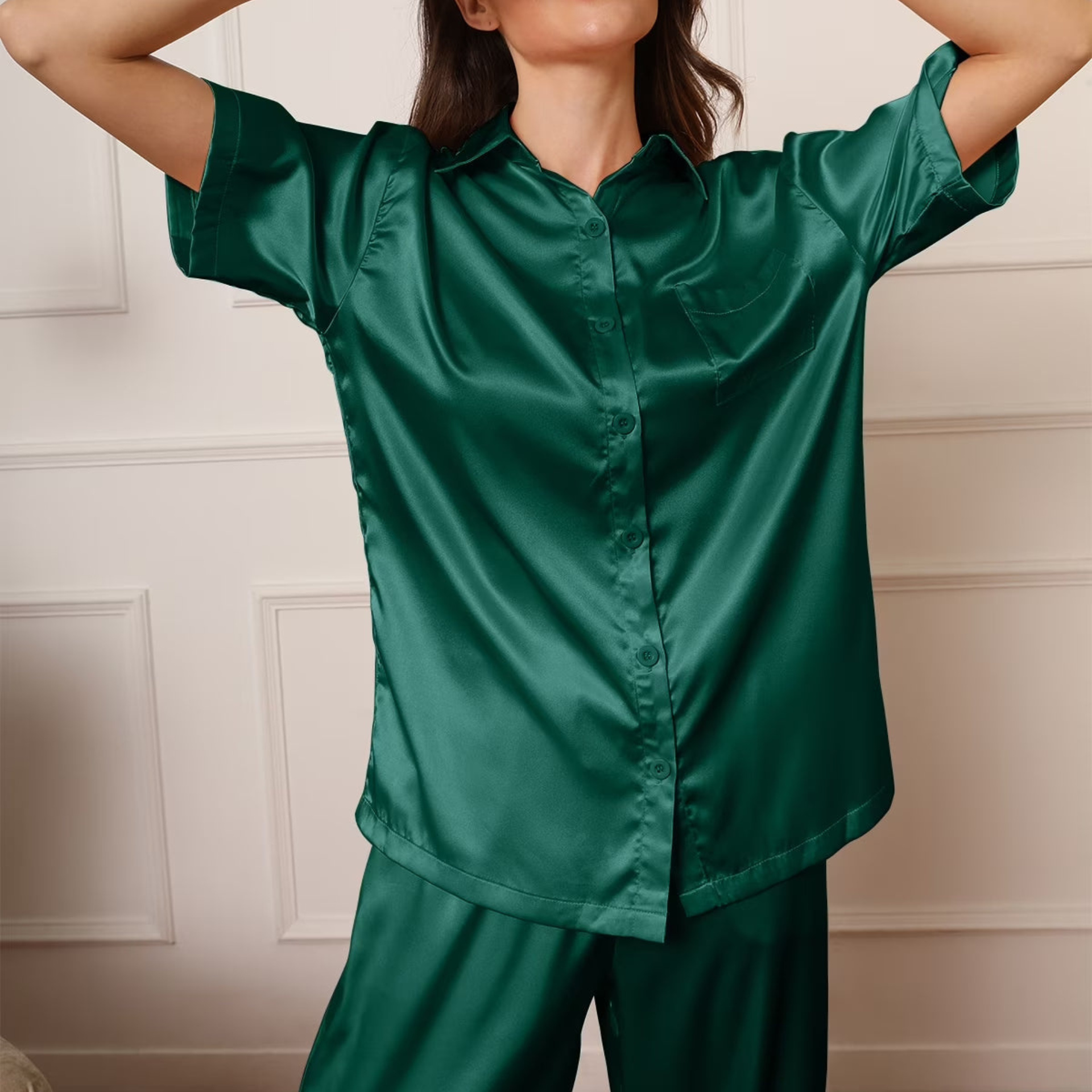 Person wearing a green satin shirt and pants set against a neutral wall.
