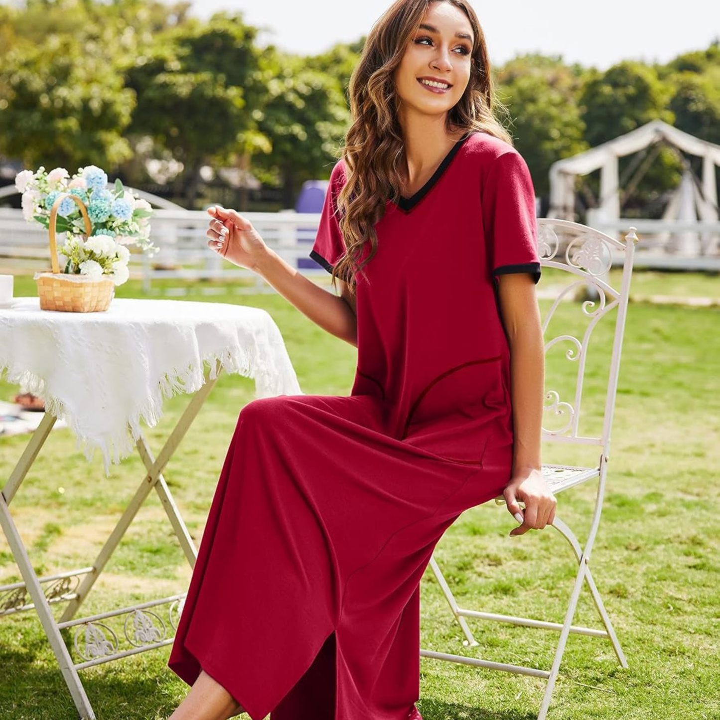 Woman in a red dress sitting outdoors with a table and flowers in the background