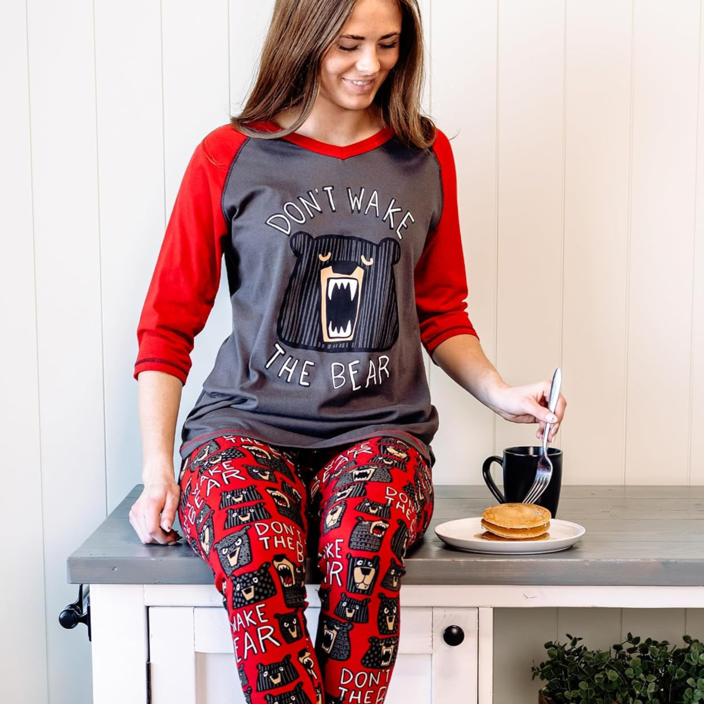 Woman wearing a 'Don't Wake the Bear' pajama set, sitting at a table with a plate of food.