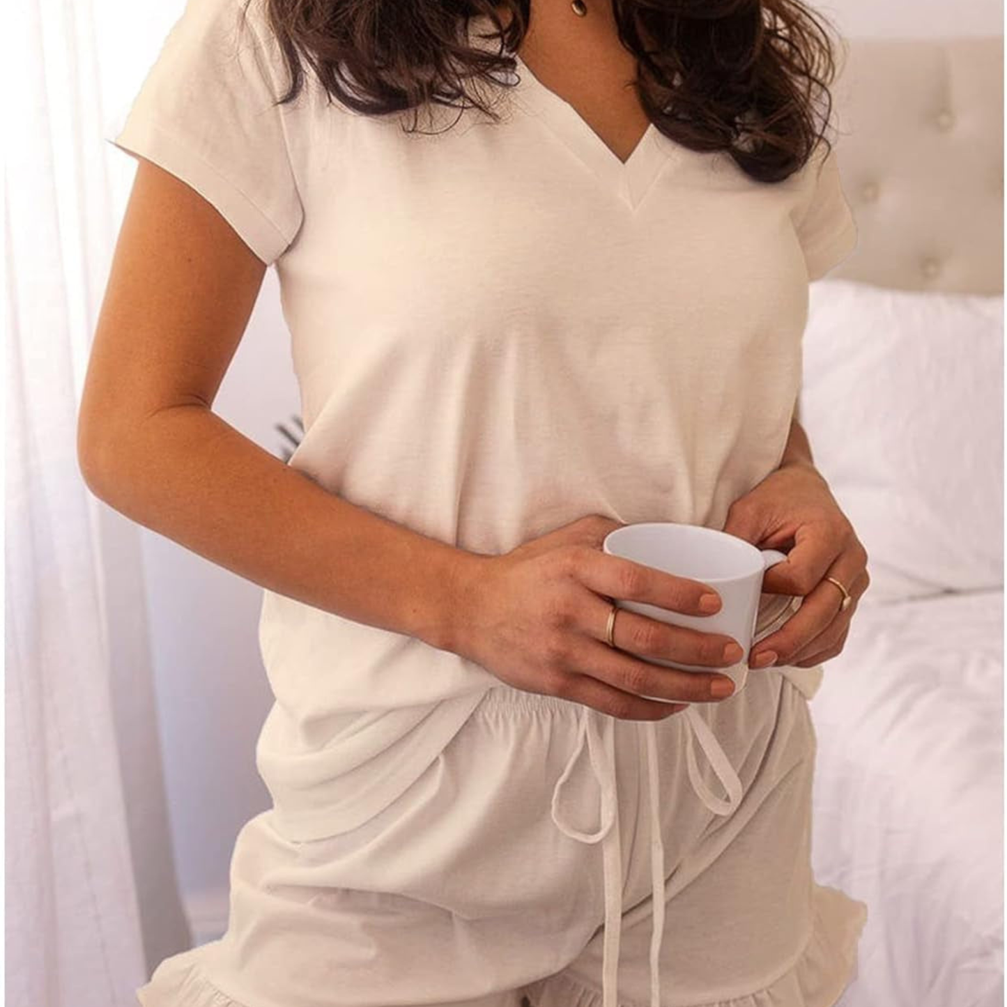 Person wearing a white outfit holding a cup in a bedroom setting