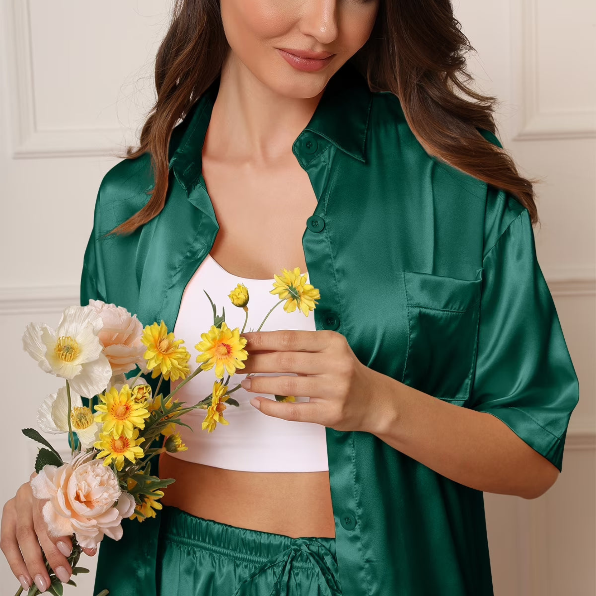 Woman in green satin robe holding flowers against a neutral background