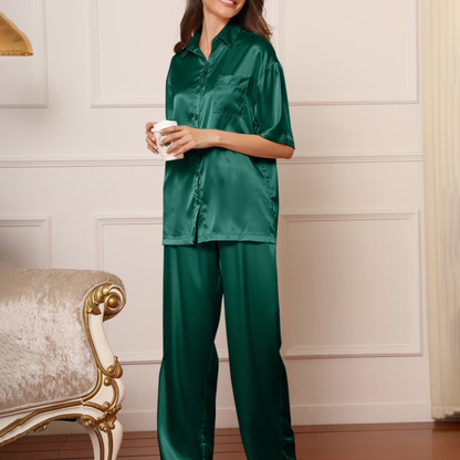 Woman wearing green satin pajamas holding a cup in a room with decorative wall paneling.
