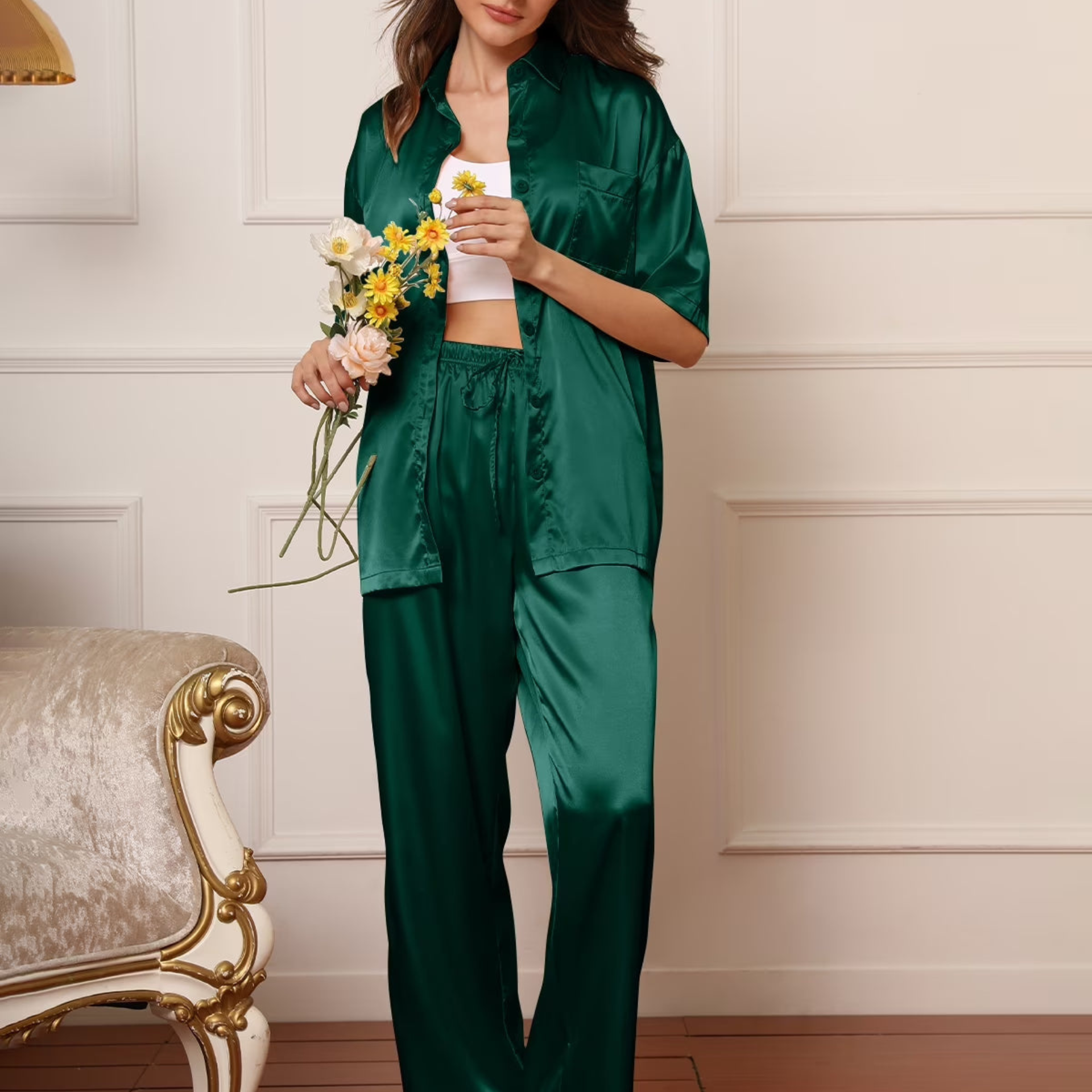 Woman in a green satin outfit holding flowers in a room with a decorative chair.