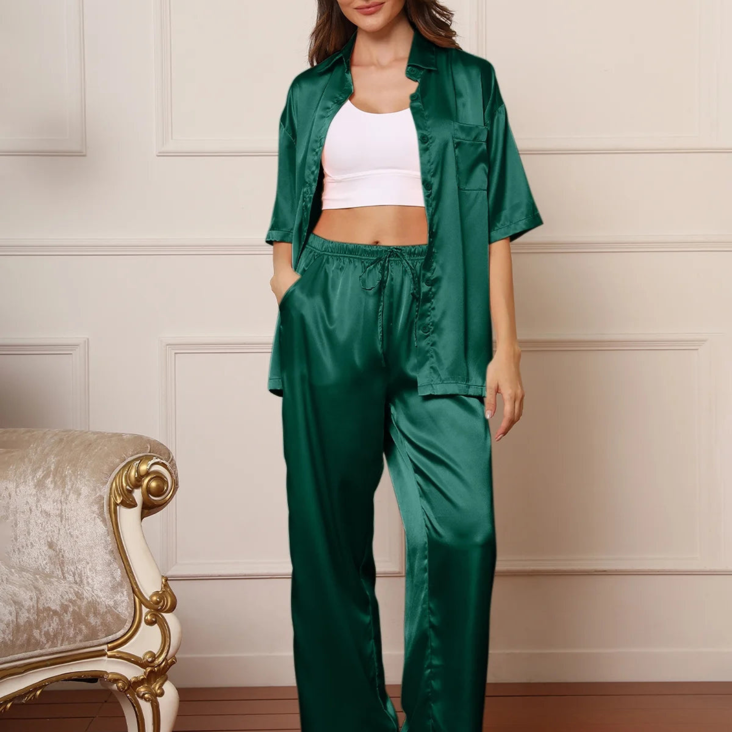 Woman wearing a green satin outfit with a white top against a neutral wall.